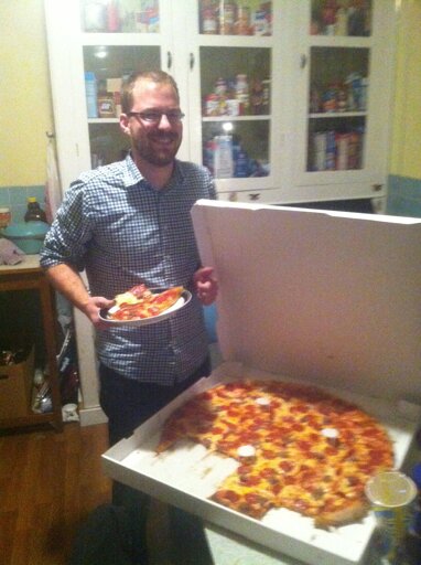 A small man standing next to an abnormally large pizza.